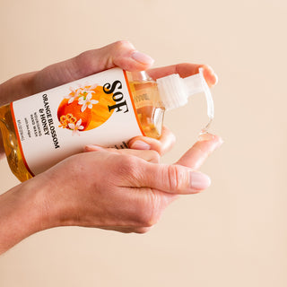 Someone pumps clear, paraben-free Orange Blossom & Honey Nourishing Hand Wash onto their finger from a dispenser bottle against a beige background.