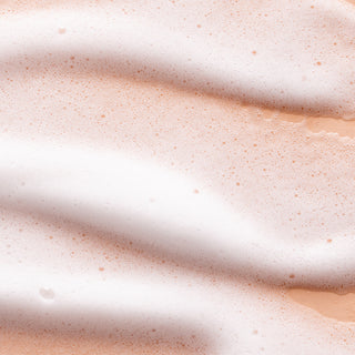 Close-up of soft, white foam bubbles on a light peach surface, forming gentle waves—a soothing texture ideal for daily cleansing with Lemon Verbena Foaming Hand Soap and Bar Soap.