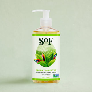 A clear pump bottle of Green Tea Leaves Nourishing Hand Wash, enriched with essential oils, features a label with green tea leaves and colorful flowers on a light green background.