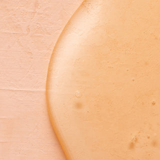 A close-up of a peach-colored textured surface with glossy, semi-transparent Shea Butter Nourishing Hand Wash—infused with essential oils—spread over it, highlighting small bubbles and texture variations.