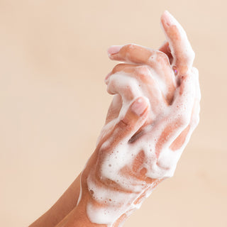 Two hands lathered with white foam from Shea Butter Liquid Hand Soap and Bar Soap are shown against a plain beige background, demonstrating gentle cleansing for ultimate handwashing and cleanliness.
