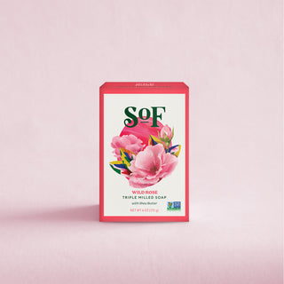 A pink box of Wild Rose Moisturizing Bar Soap with organic shea butter, decorated with pink rose illustrations, sits on a light pink background and promises a rich, moisturizing lather.