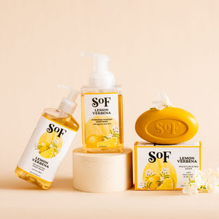 The Lemon Verbena Bundle—liquid soap, foaming hand wash, and bar soap—sits on a beige background. Citrus designs, layered scents, and white floral accents highlight the packaging for a fresh daily cleanse.